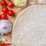 Pizza base with fresh tomatoes and garlic on the side