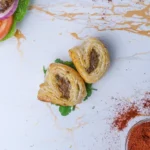 Two mini halal sausage rolls with a burger and some spices on a table